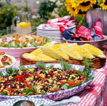 Photo of picnic foods, including corn & bean salad, on a picnic table.