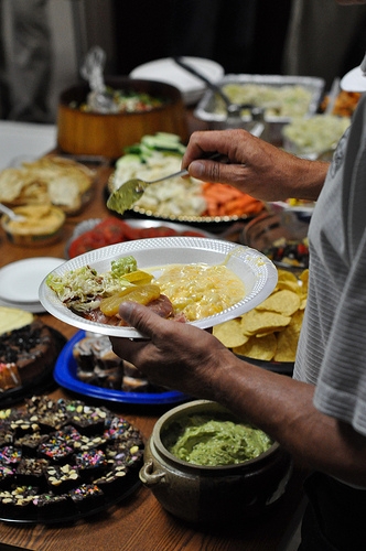 A person's hand putting food on their plate at a potluck.