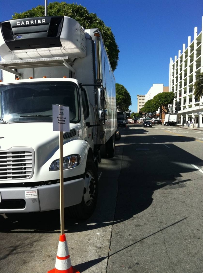Delivery truck on side of city street, behind sign and traffic cone designating the parking space.